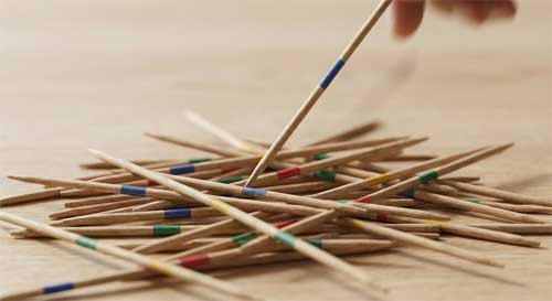 Montón desordenado de palillos de madera finos con bandas de colores, mostrando la tensión del juego Mikado