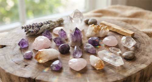 Colección de cristales brillantes de diferentes colores (amatista, cuarzo rosa, citrino) dispuestos armoniosamente sobre una superficie de madera natural, reflejando luz suave