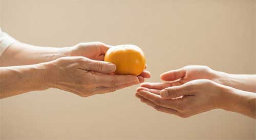 Manos extendidas ofreciendo una fruta con respeto frente a manos vacías que reciben con gratitud, simbolizando la generosidad opuesta al robo