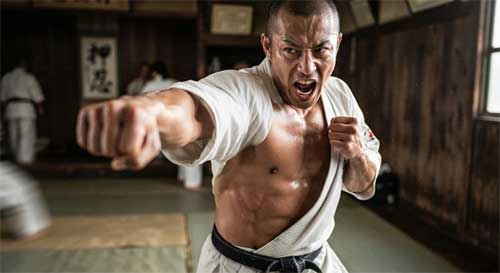 Practicante de Kyokushin ejecutando un golpe de puño corto y directo al torso, demostrando tensión muscular extrema y foco intenso